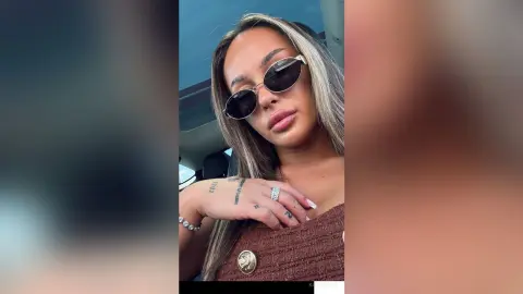 KaylaDepp poses in a car wearing dark sunglasses and a brown textured top, showing off her long blonde-highlighted hair and hand tattoos.