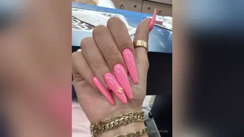 Close-up of long pink almond-shaped manicured nails with gold ring accents on a woman's hand.