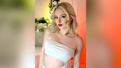 Blonde woman in a white strapless top posing in a bright, modern room with a soft aesthetic mood.