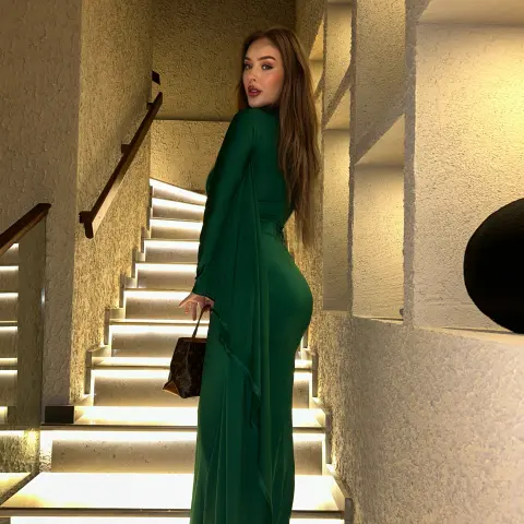 Elegant woman in a long emerald green gown posing on a modern lit staircase for a sophisticated evening look.