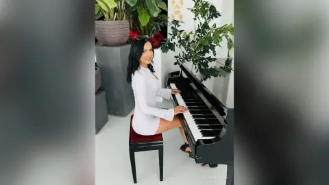 Elegant woman in a white dress sitting by a black grand piano in a bright, modern room with indoor plants.