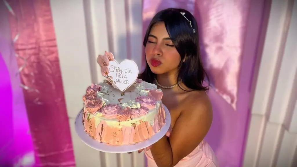 Young woman in blue bikini and pearl necklace posing under dreamy purple lighting in a marble bathroom.