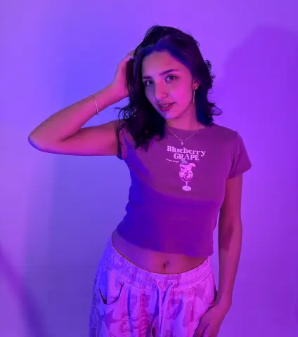 Young woman in a purple graphic t-shirt posing against a dreamy lavender background with moody lighting.