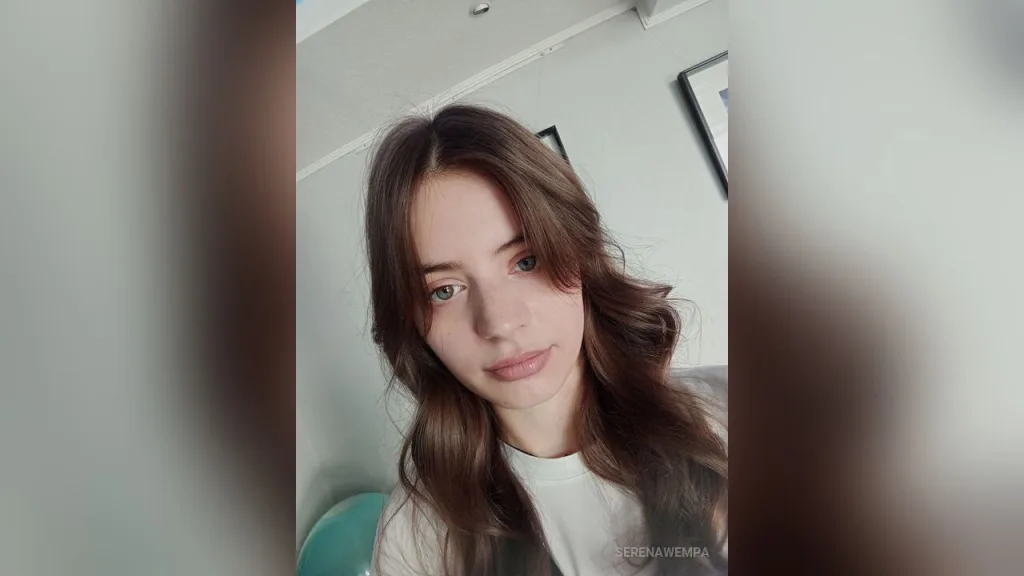 Close-up portrait of a young woman with long brown hair and green eyes looking calmly at the camera.