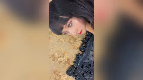 Young woman with dark bangs and red lipstick posing in a vintage floral setting with an ornate black frame.
