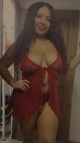 Smiling woman in a red lace chemise nightgown posing indoors with long curly hair.