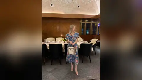 Elegant woman in a blue floral midi dress posing in a sophisticated restaurant setting.