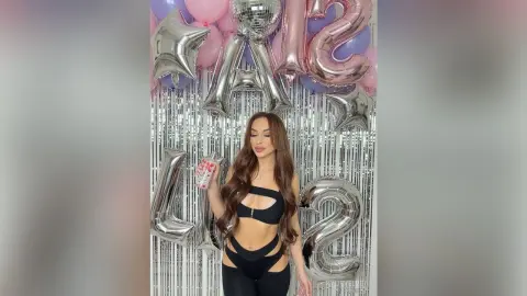 Glamorous woman in a black cutout bodysuit celebrating at a birthday party with silver balloons and tinsel.