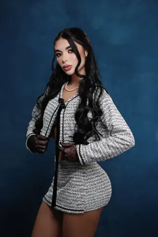 Elegant woman in a stylish black and white tweed skirt suit posing against a deep blue studio background.