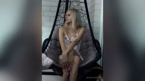 JaunitaHereth sits in a hanging chair wearing a white lace slip, looking away with her blonde hair down.