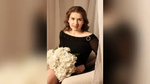 Elegant woman in a black evening dress holding a large white hydrangea bouquet in a soft, dreamy setting.