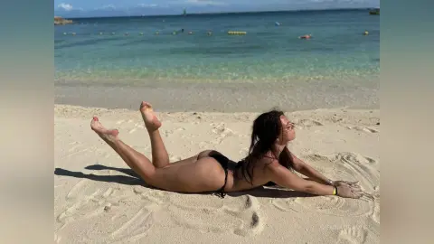 Young woman in a black bikini relaxing on a sunny beach by the turquoise ocean water.