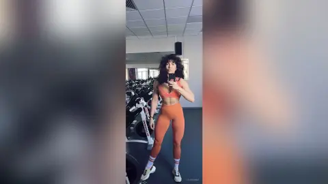 Fit woman in orange gym set taking a selfie in a modern fitness center gym.