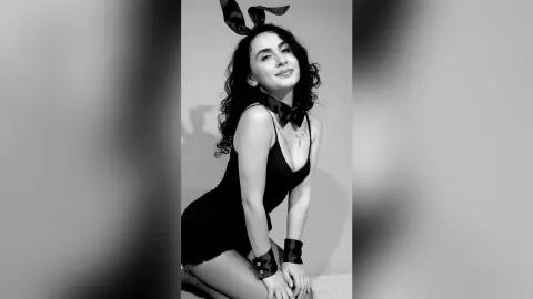 Smiling woman in a black bunny ear outfit posing in a minimalist studio setting for a playful portrait.