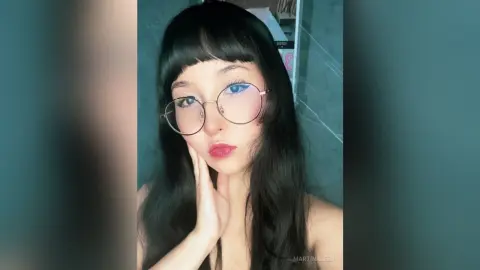 Young woman with black bangs and round glasses posing for a moody portrait in a modern setting.