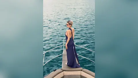 Elegant woman in a navy blue backless maxi dress standing on a luxury boat in turquoise ocean water.