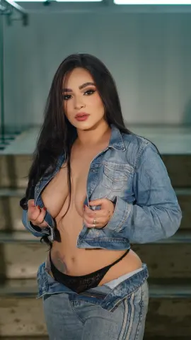 Young woman in denim jacket and jeans posing on stairs with a confident, casual mood.