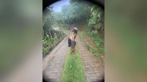 Young woman in a black bikini walking along a lush, tropical forest path on a misty summer day.
