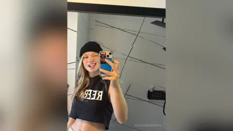 SilviaPrespertys takes a playful mirror selfie wearing a black beanie and a black crop top in a modern bathroom.