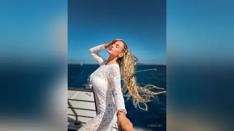 Blonde woman in a white lace dress enjoying a sunny day on a boat in the blue ocean.