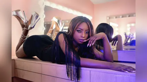 Glamorous woman in a black fringed dress lounging in a pink vanity room with silver high heels.