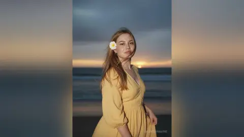 ShantayMayne poses on a beach at sunset wearing a yellow v-neck dress with her long hair down.