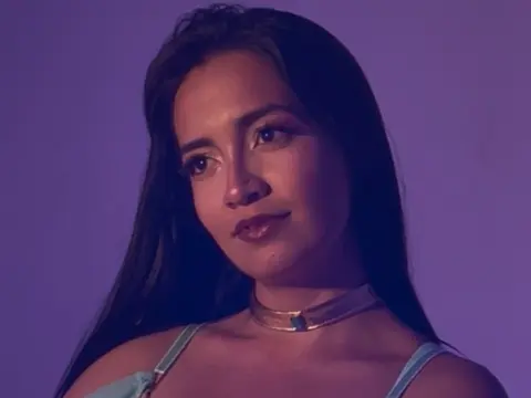 Portrait of a woman with long dark hair wearing a gold choker against a moody purple background.