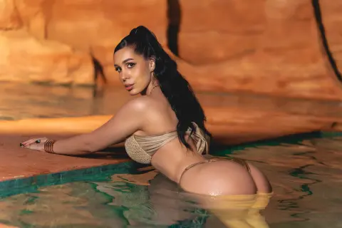 Glamorous woman in a gold bikini relaxing in a warm desert oasis pool at sunset.