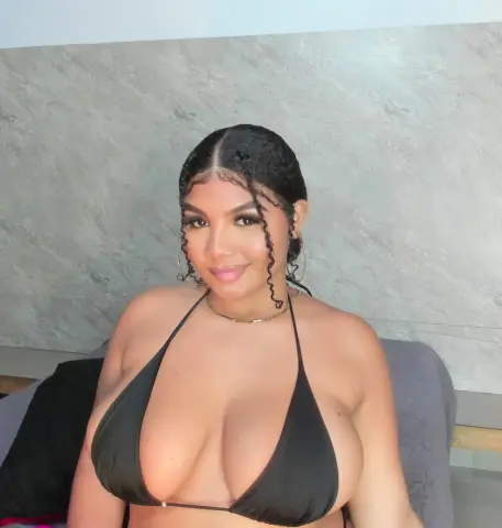 Smiling woman with curly dark hair wearing a black string bikini top in a modern indoor setting.
