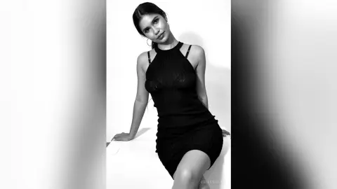 Elegant woman in a black halter neck cocktail dress posing against a white background in a moody black and white portrait.