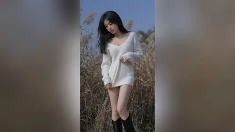 Young woman in a cozy white knit sweater posing in a dreamy field of tall dried grass under a soft blue sky.