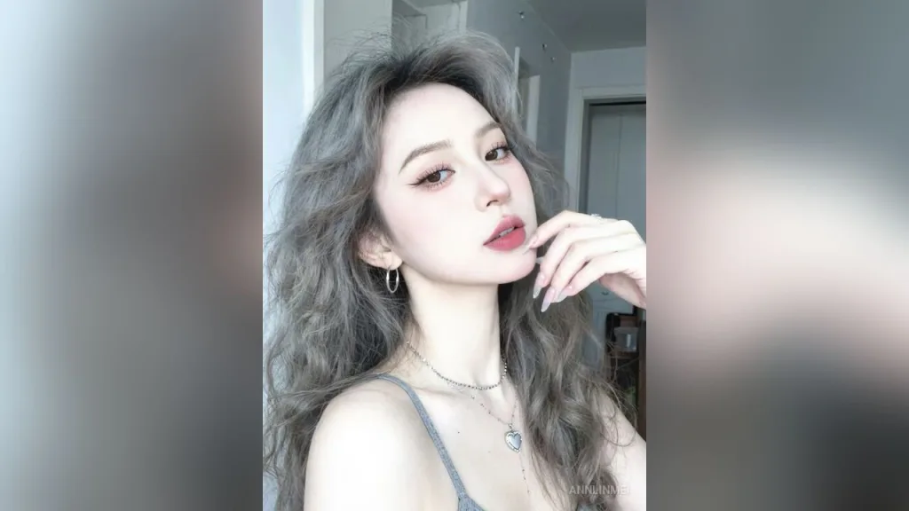 AnnLinMei — AnnLinMei poses with long wavy grey hair and silver jewelry in a grey tank top.