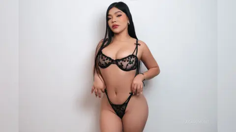 Young woman in black floral lace lingerie posing confidently against a plain white background.