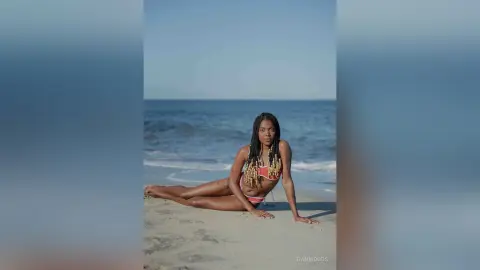 Young woman in a red bikini relaxing on a sunny beach with ocean waves in the background.