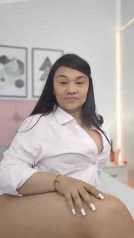 Smiling woman in a white button-down shirt relaxing in a bright, modern bedroom setting.