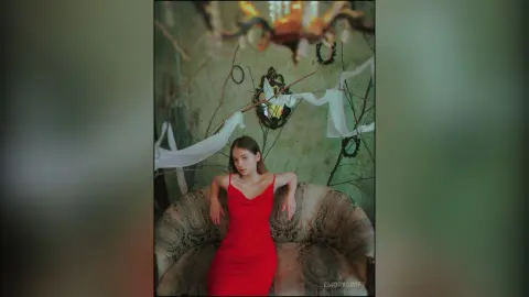 EmorySwift wearing a red dress while sitting in a large, rounded chair against a textured green wall.