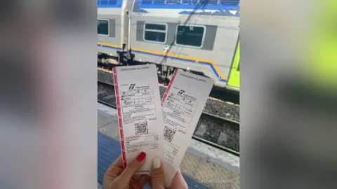 Two Trenitalia train tickets held in front of a modern silver passenger train at a railway station platform.