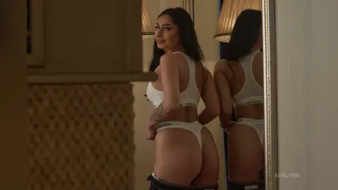 AvaLynn poses in white Calvin Klein underwear, showing her bare back and buttocks while looking over her shoulder in a mirror.