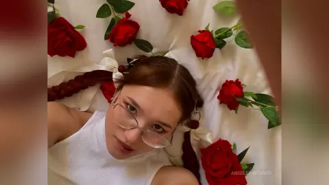 Young woman in a white ribbed top lying among red roses for a romantic and aesthetic portrait.