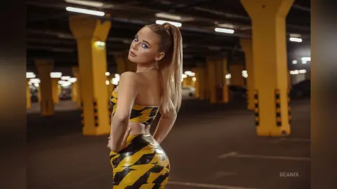 BeaNix poses in a yellow and black patterned outfit, looking over her shoulder with her blonde hair in a high ponytail.