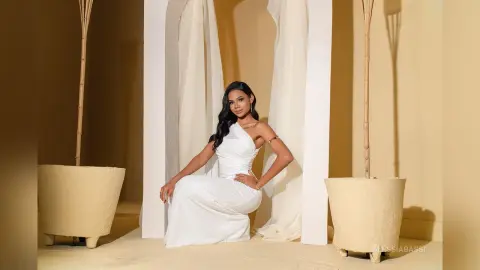 Elegant woman in a white silk gown posing in a minimalist beige studio setting with a serene mood.