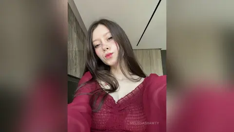 Young woman in a red ruffled blouse posing with a soft expression in a modern indoor setting.