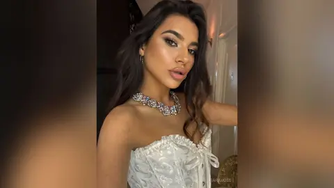 Glamorous woman in a white corset and statement crystal necklace posing for a glowing selfie.
