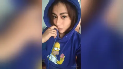 Young woman in a blue Simpsons graphic hoodie posing indoors with a cozy, casual mood.