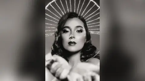 Elegant woman in vintage glamorous attire wearing a sparkling sunburst halo headpiece in a moody portrait.
