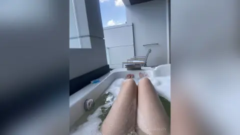 EllieFrosty reclines in a white bathtub filled with soapy white bubbles, showing her bare legs and feet.