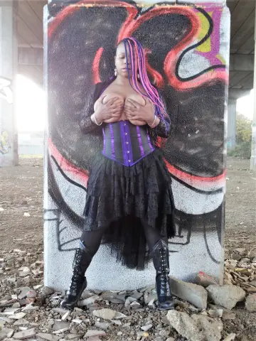 Woman in black gothic corset and ruffled skirt posing against colorful street art graffiti.