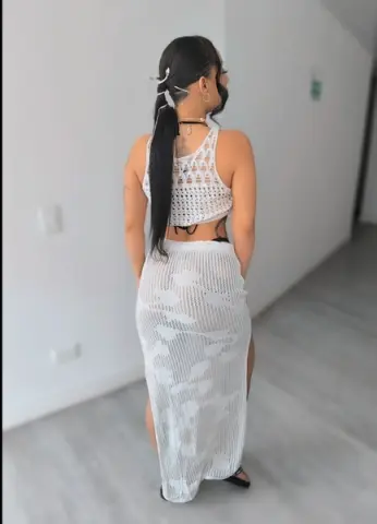 Woman in white crochet crop top and matching maxi skirt standing in a minimalist bright room.