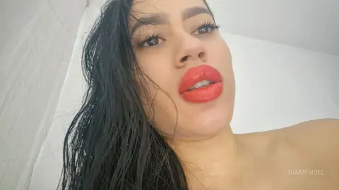 Close-up portrait of a young woman with long dark hair and bright red lipstick in a bright indoor setting.