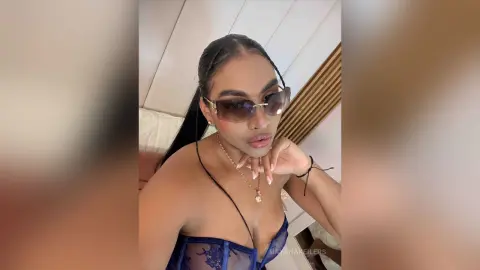 Stylish woman in a blue lace corset and sunglasses posing indoors with a confident, glamorous mood.